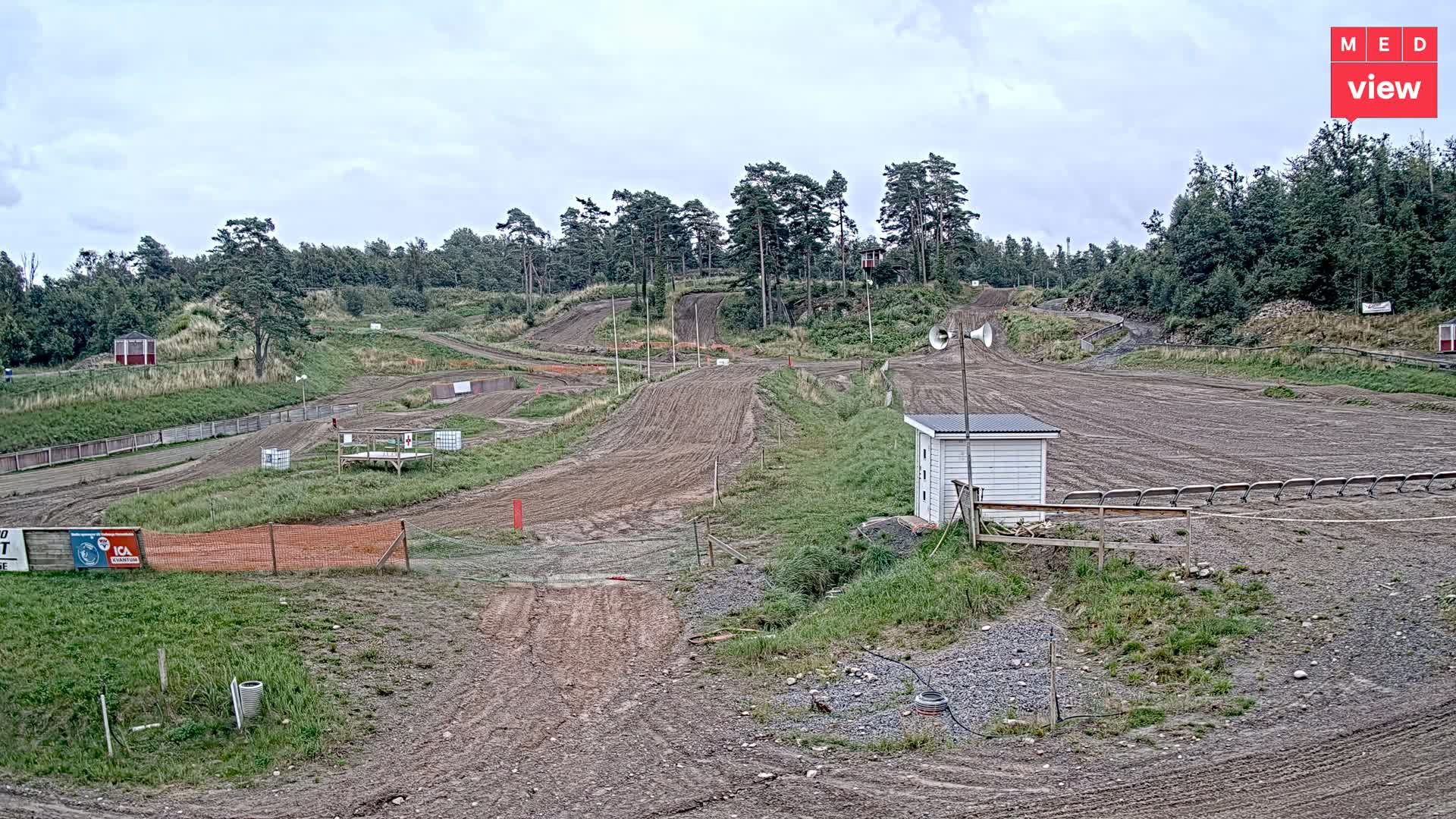 A dirt motocross track with several turns and jumps is surrounded by trees under an overcast sky.