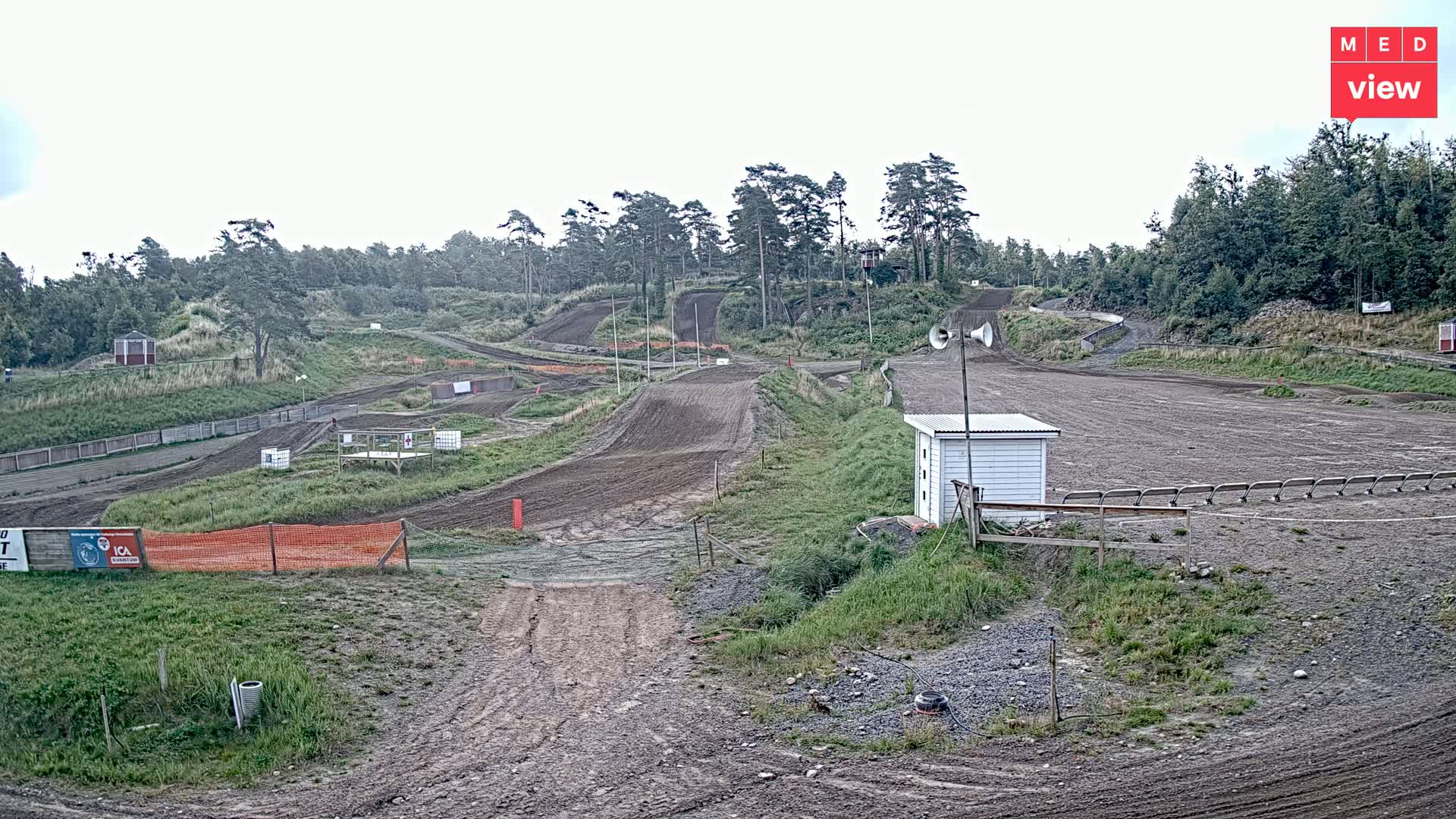 A motocross track, mostly dirt, winds through a grassy area, under an overcast sky.