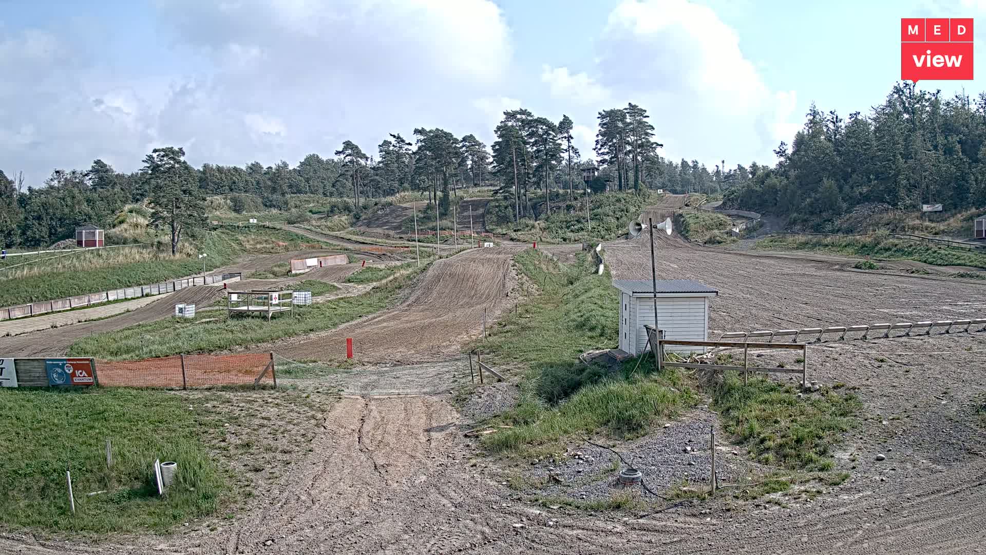 A motocross track, mostly dirt, winds through a grassy area, under an overcast sky.