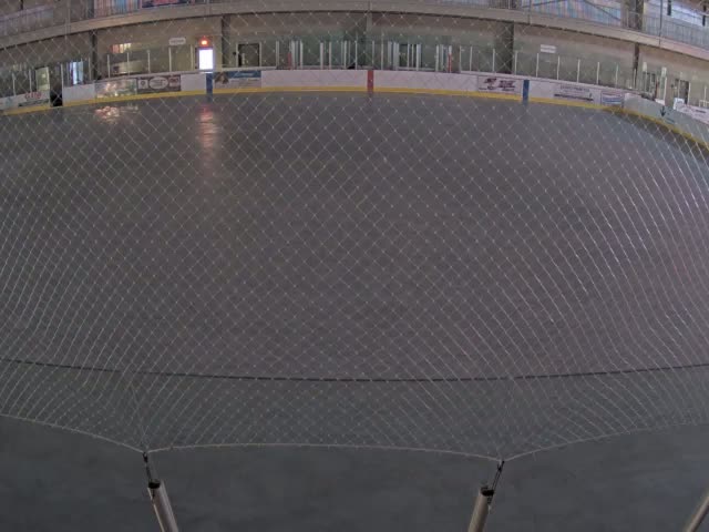 A view through a net reveals an empty indoor ice rink.