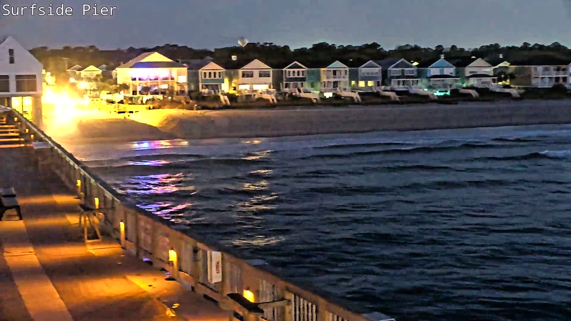 A heavily obscured and blurry night view of a coastal area, with distant lights appearing diffused through dense fog or rain on the camera lens.