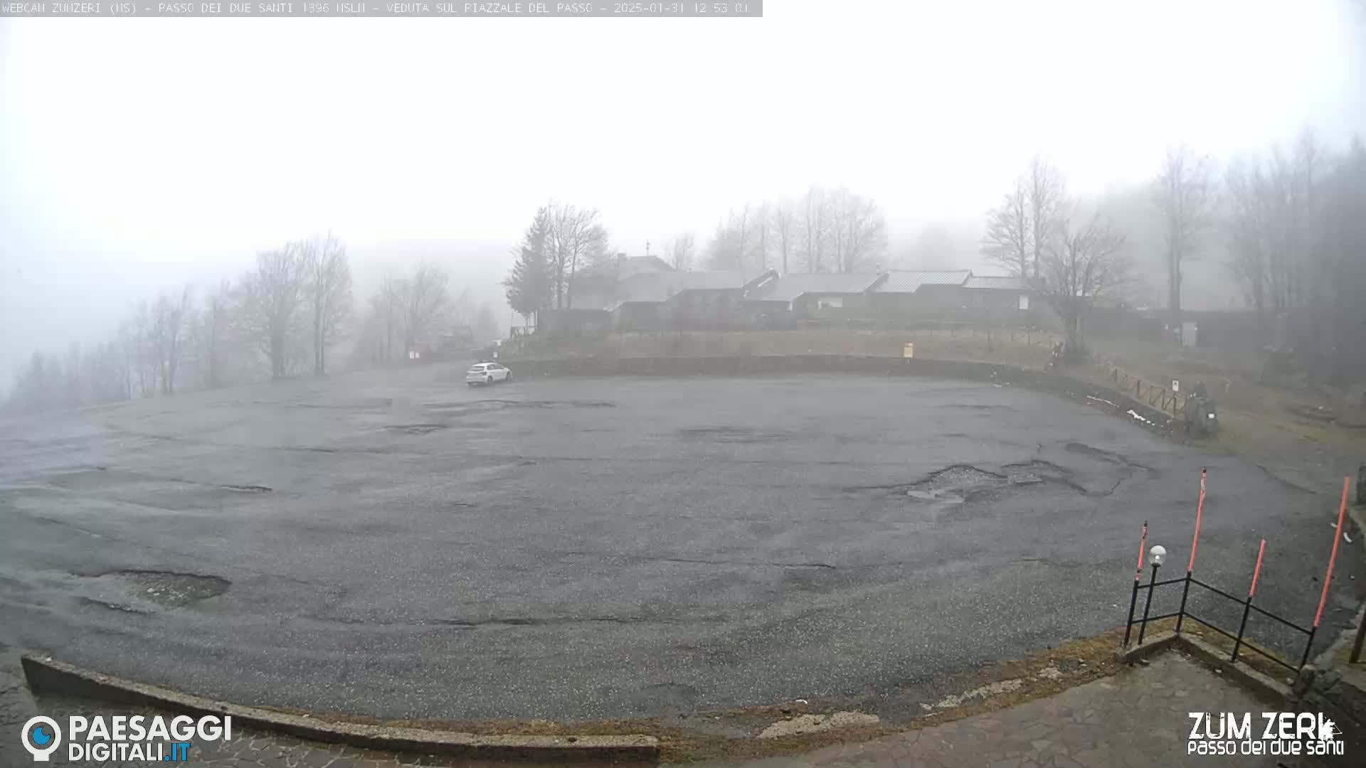 A mostly empty, damaged asphalt parking lot is visible in foggy conditions, with a few buildings and trees in the background.