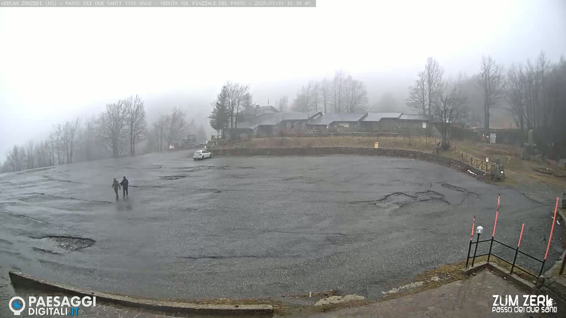 A foggy, wet parking lot with a building in the background and two people walking.