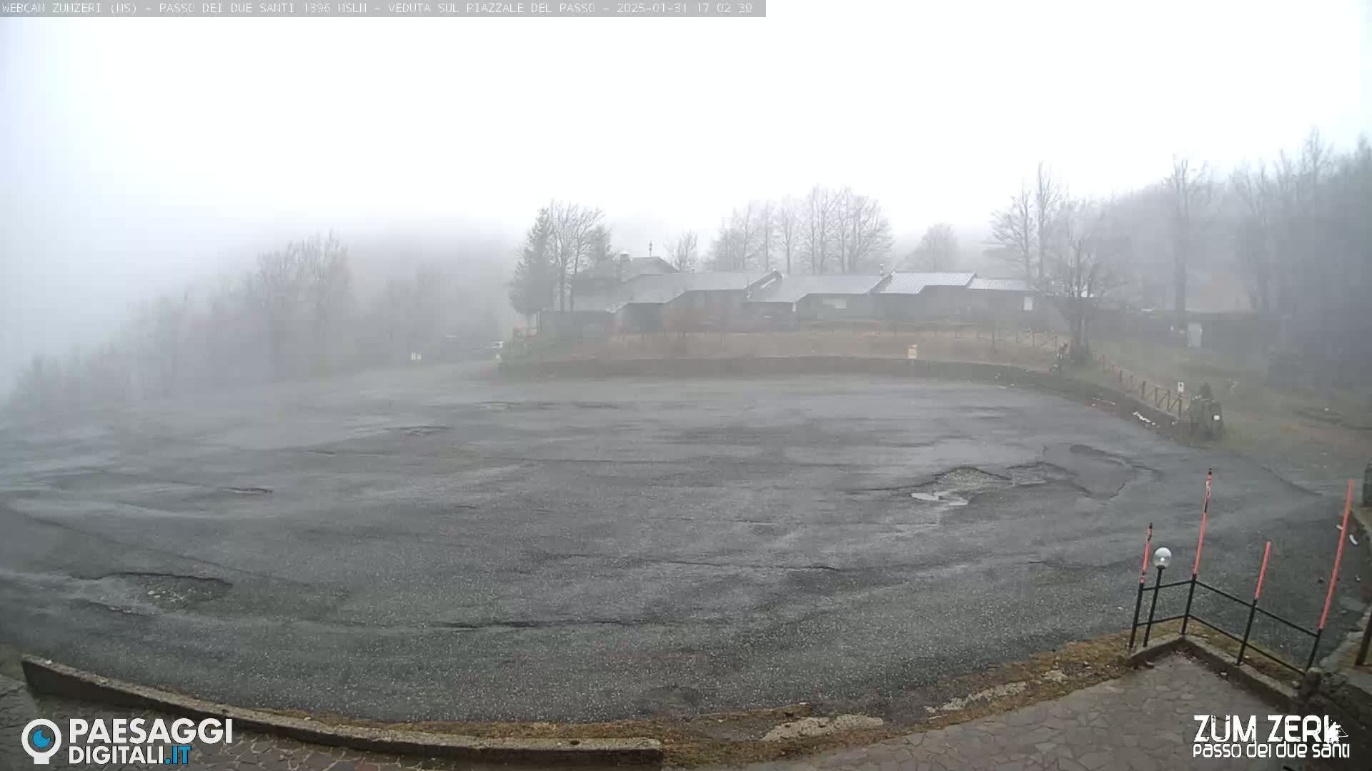 A foggy parking lot with a few buildings in the background is visible on a gray day.