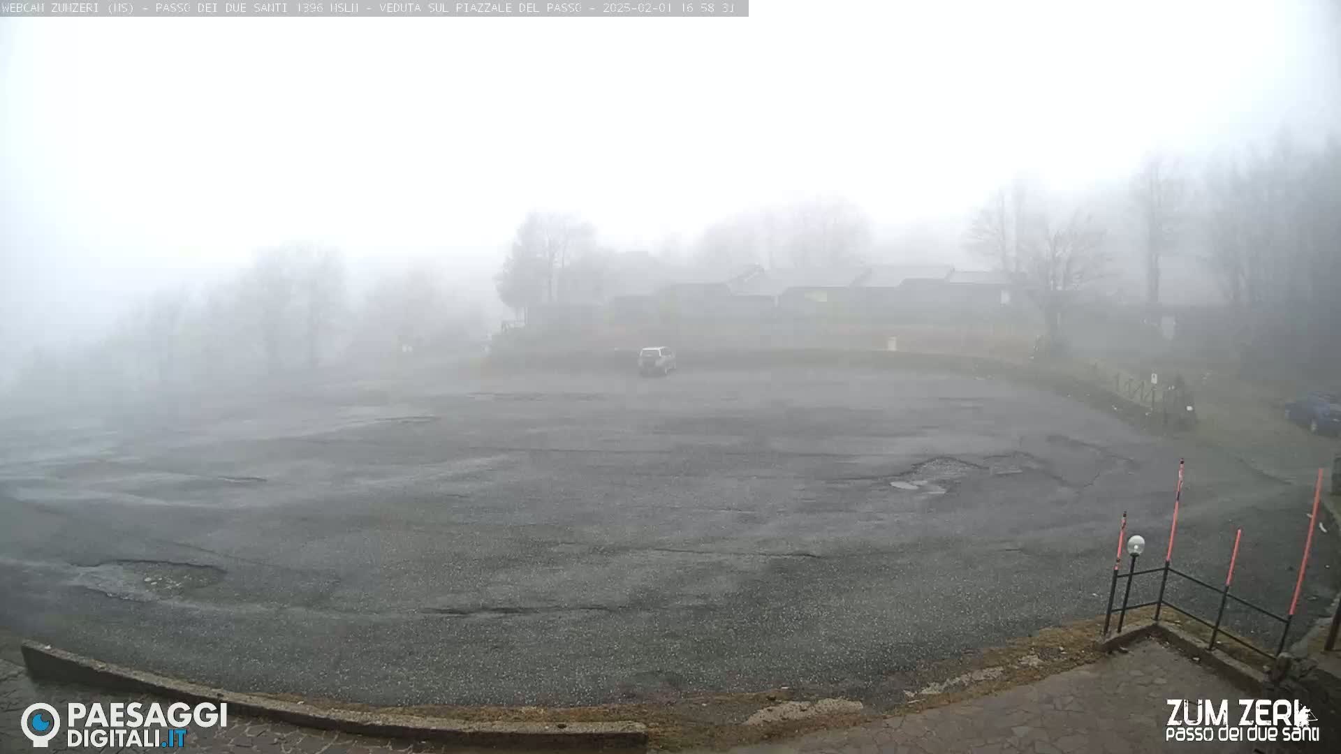 A foggy parking lot is visible, with a few trees and buildings barely discernible in the distance.