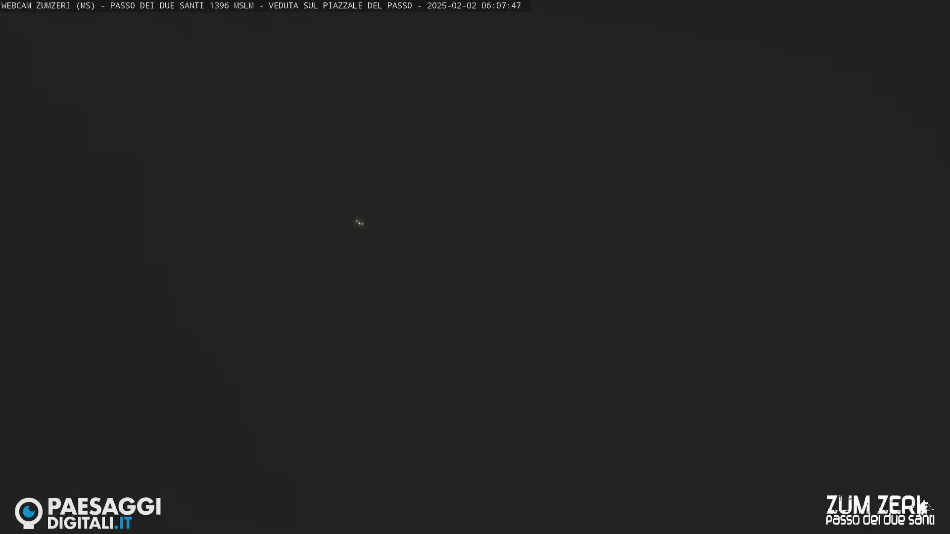 A dark, nighttime image shows a mostly black screen with a few faint lights visible in the distance.
