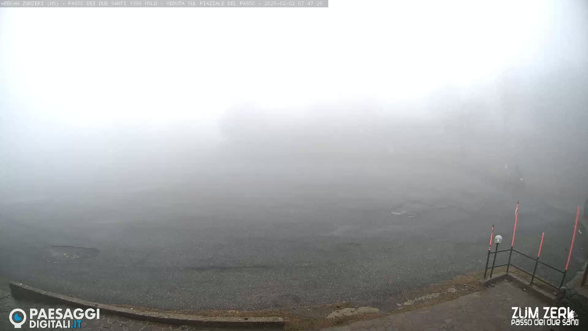 A mostly empty, dark-colored paved area is shrouded in thick fog.