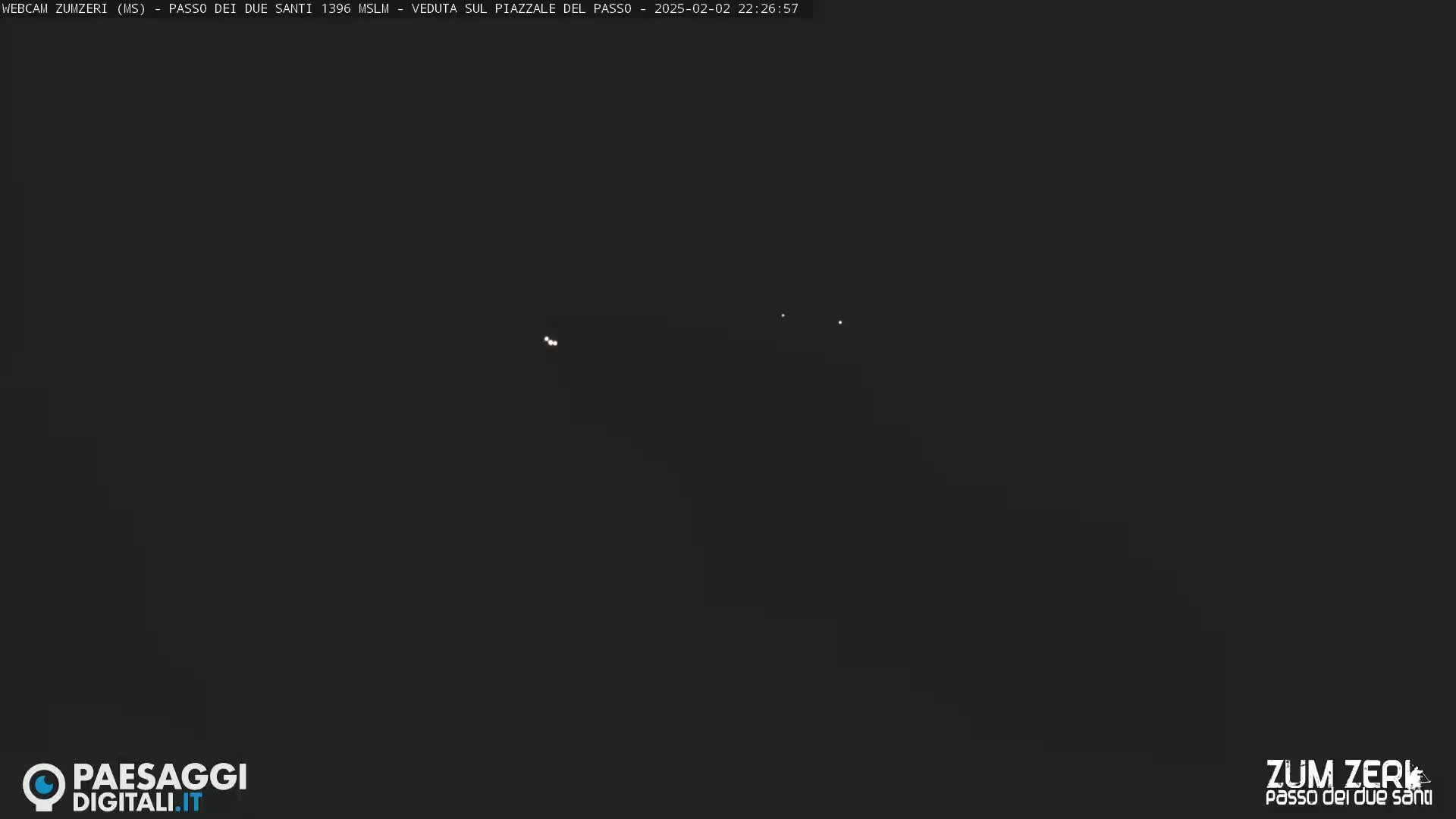 A dark, nighttime scene shows a few faint lights in the distance.