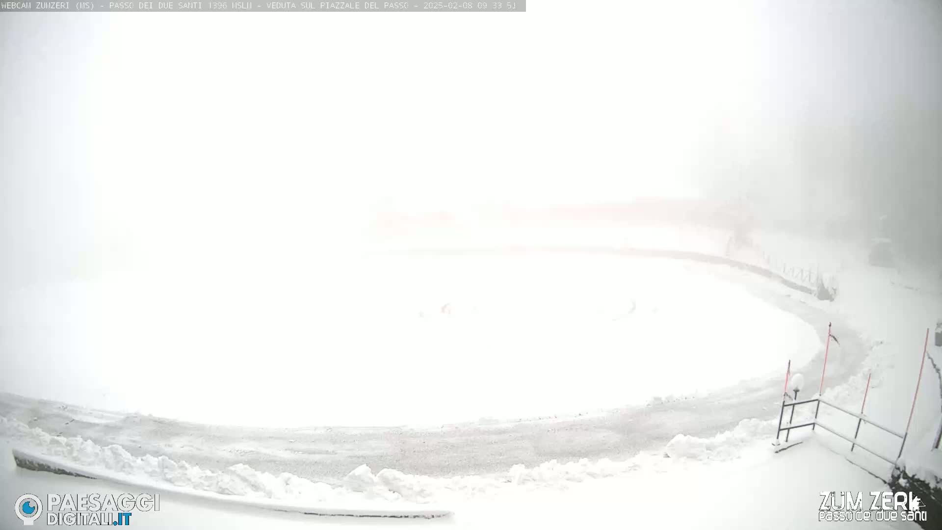 A snow-covered plaza and road are barely visible in heavy fog and snow.