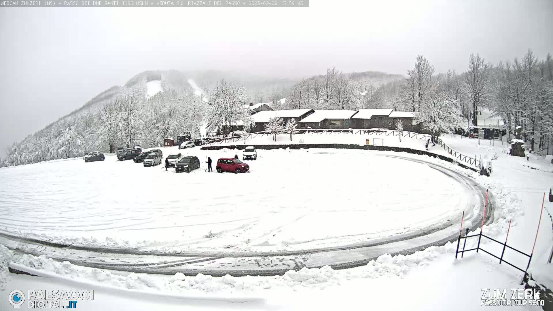 A snow-covered parking lot with several cars and a building in the background, under an overcast sky.