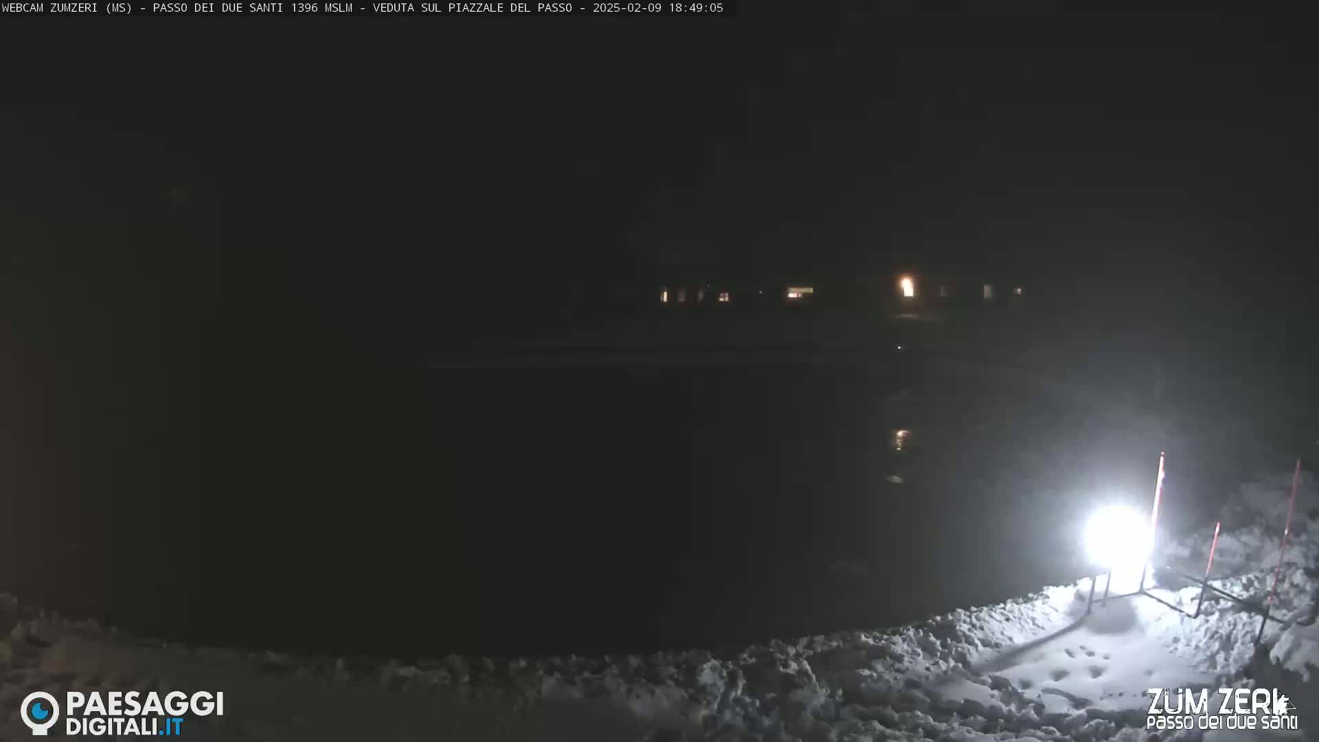 A nighttime, snow-covered scene is illuminated by a bright light source near a snowdrift.