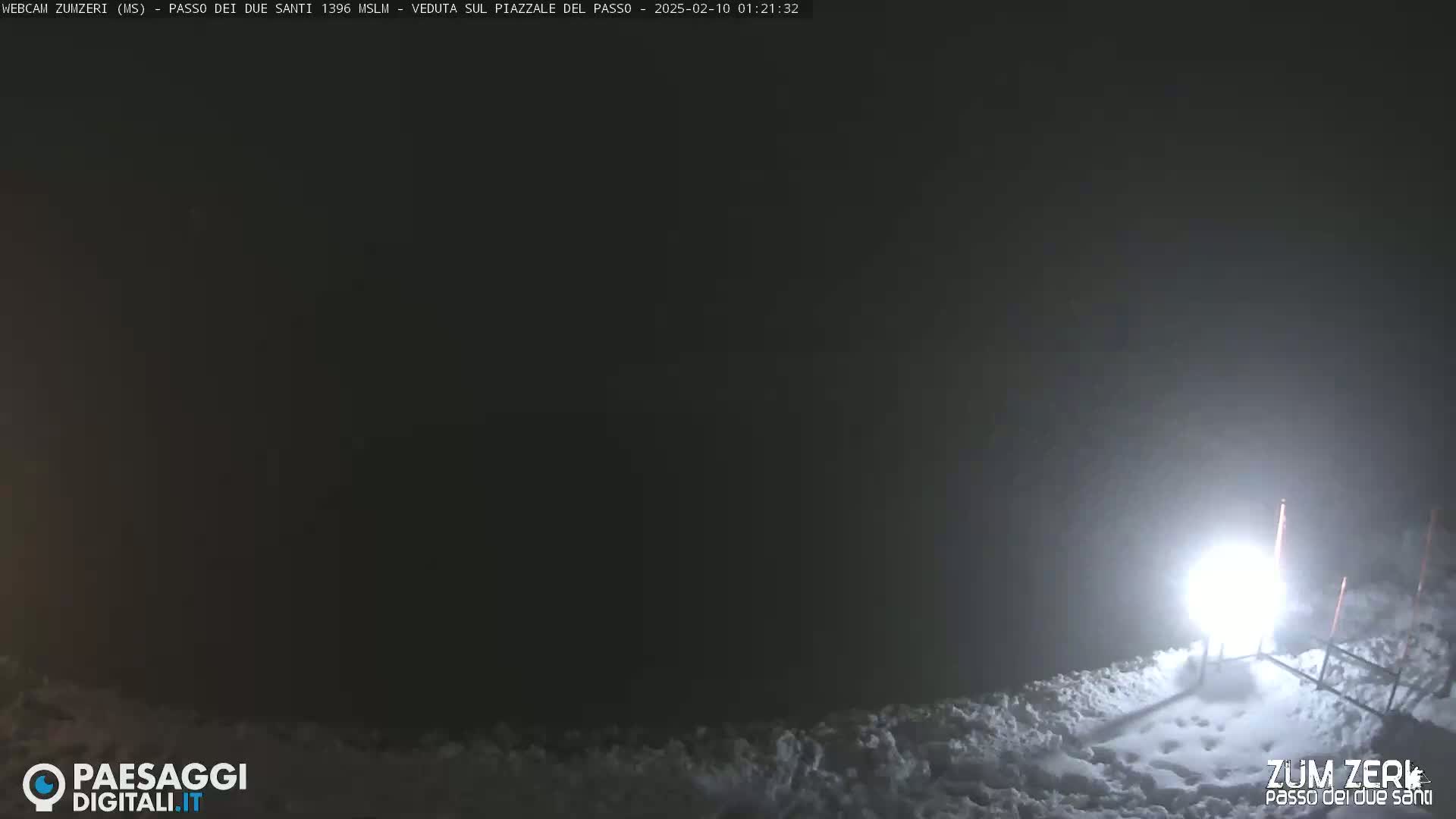 A bright light illuminates a snow-covered area at night in foggy conditions.