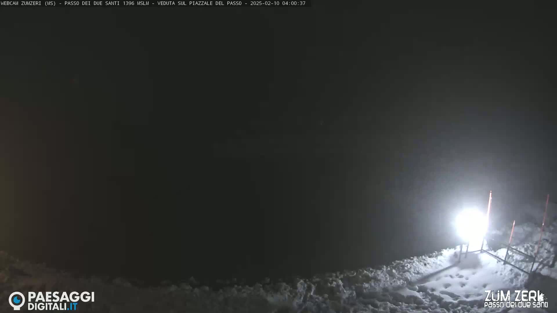 A nighttime, snowy scene is illuminated by a bright light source near a metal structure.