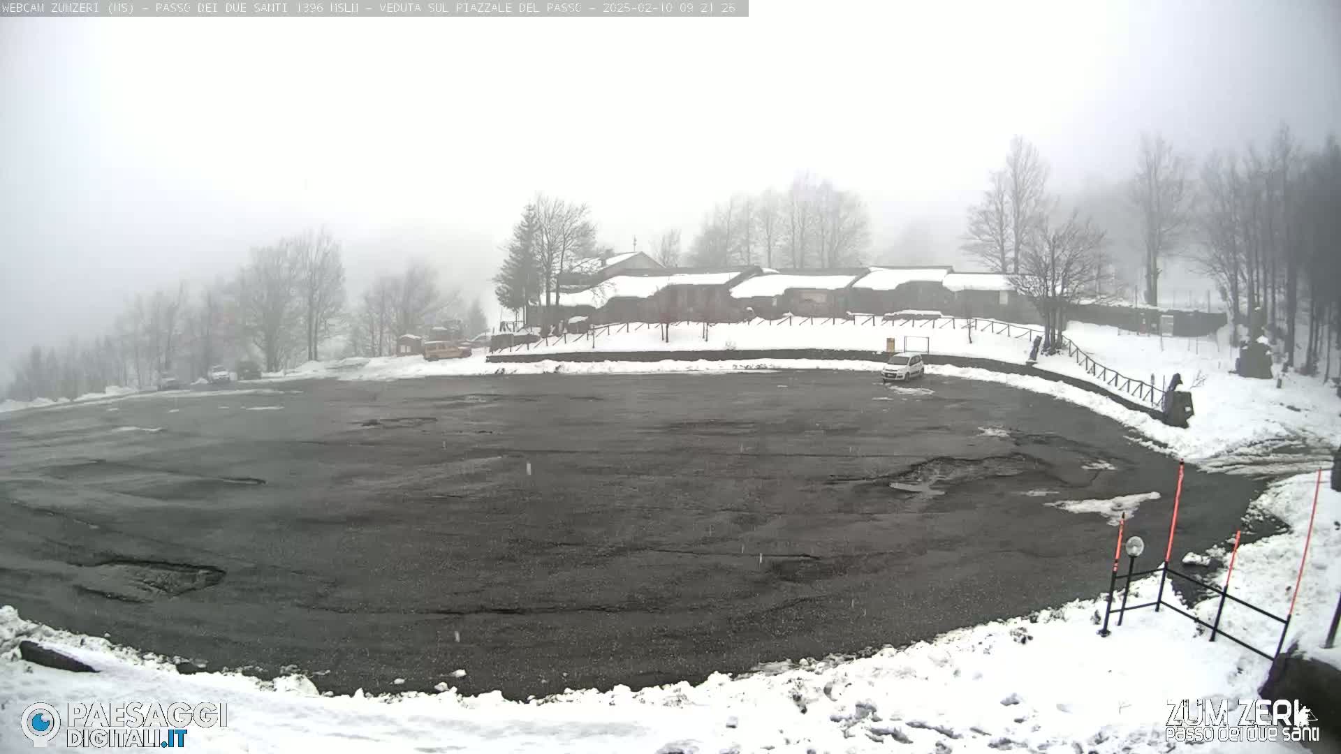 A snow-covered parking lot with a building in the background on a foggy day.