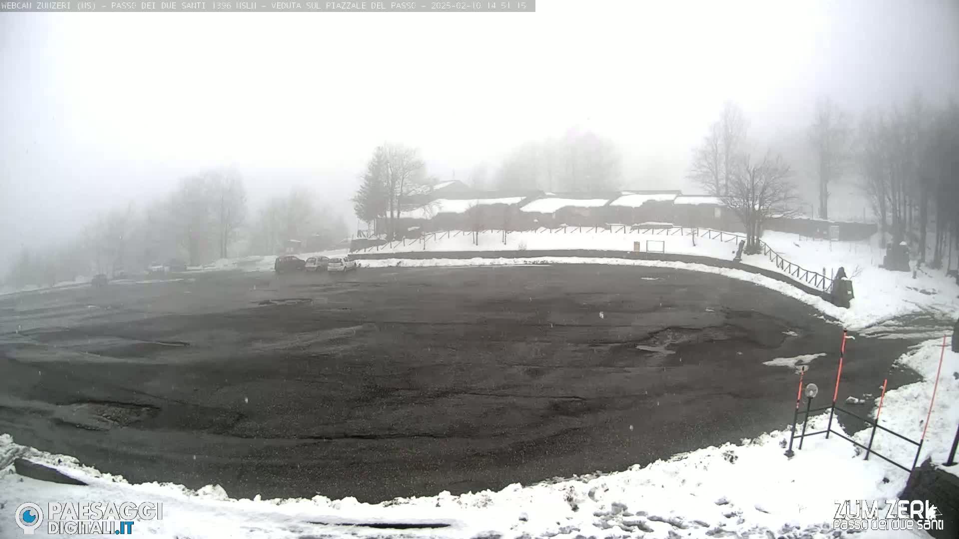 A foggy, snowy parking lot with a few cars and a building in the background.