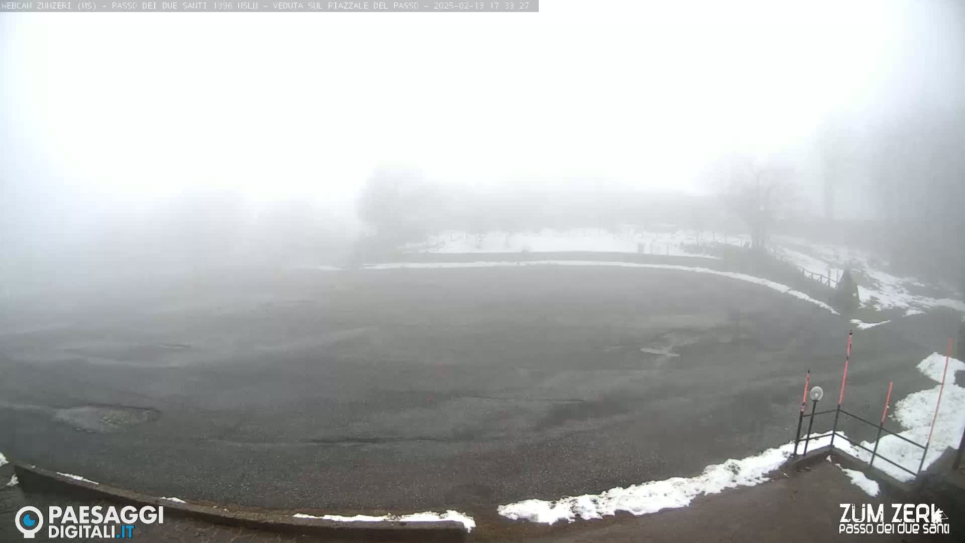 A mostly empty, dark asphalt area with patches of snow is visible through a thick fog.
