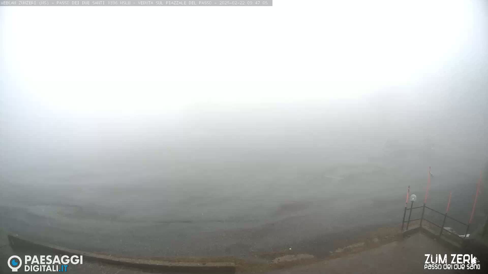 A foggy scene shows a dark gray paved area next to a body of water shrouded in mist.
