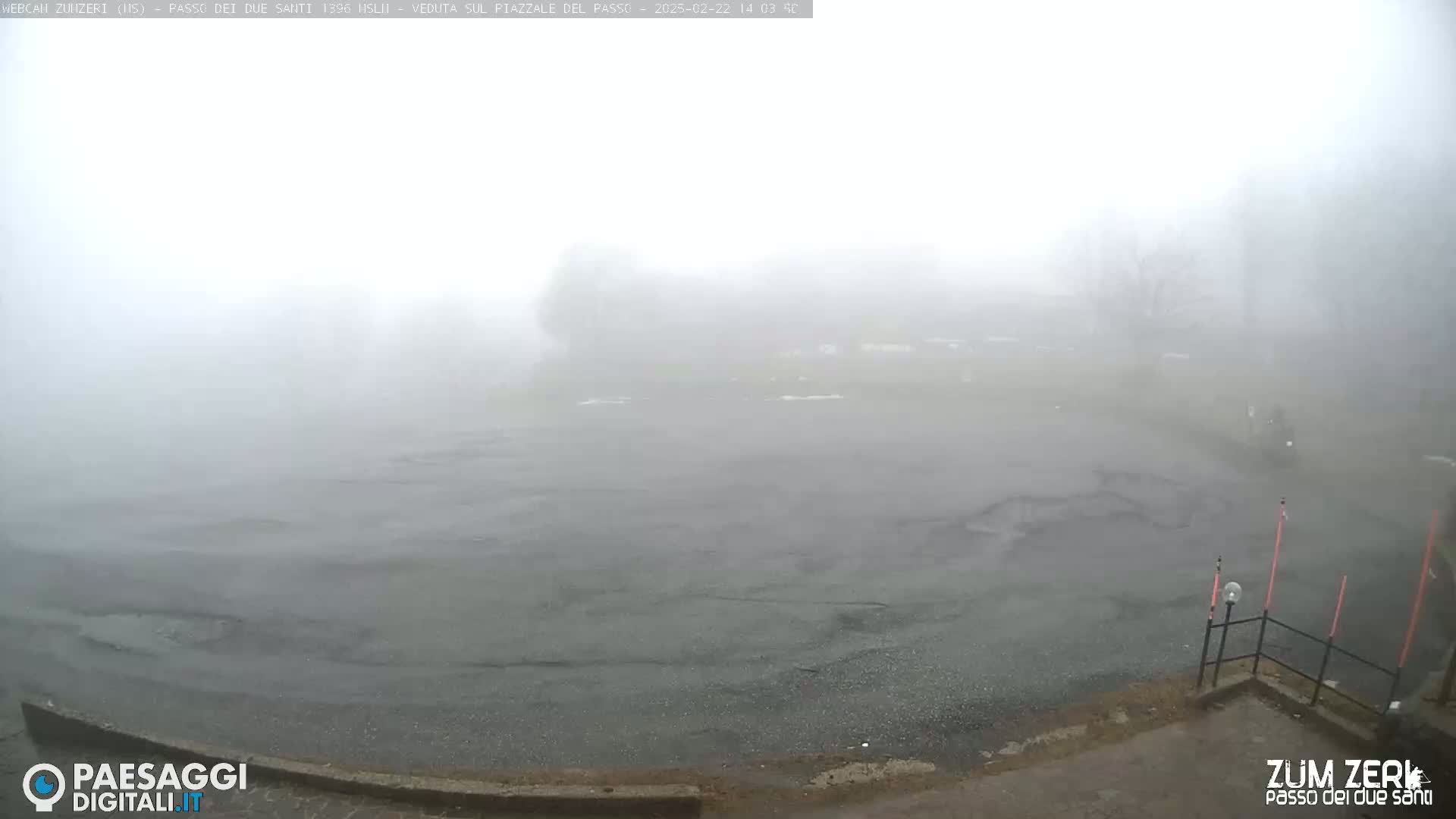 A fog-shrouded, empty asphalt plaza is visible, with muted outlines of trees and vegetation in the hazy distance.