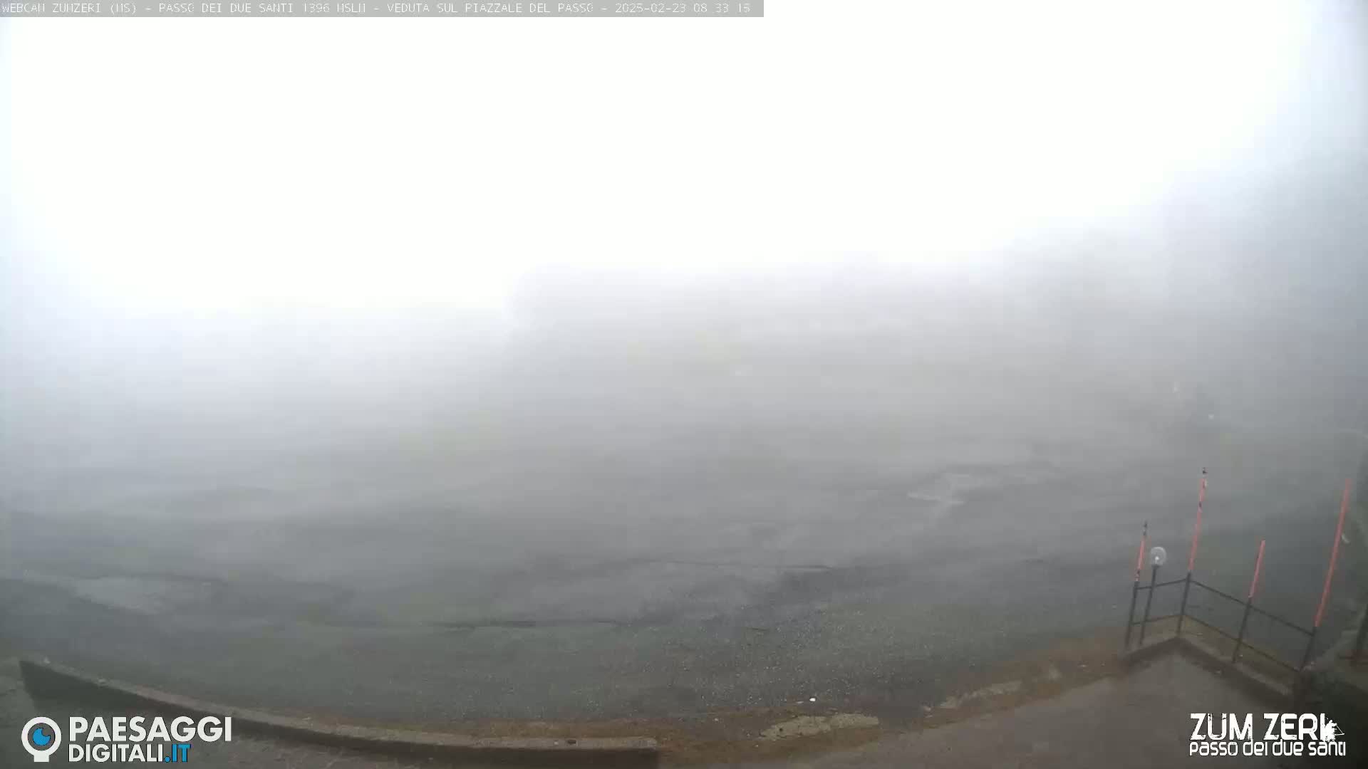 A foggy, overcast scene shows a dark gray paved area extending into a thick fog.
