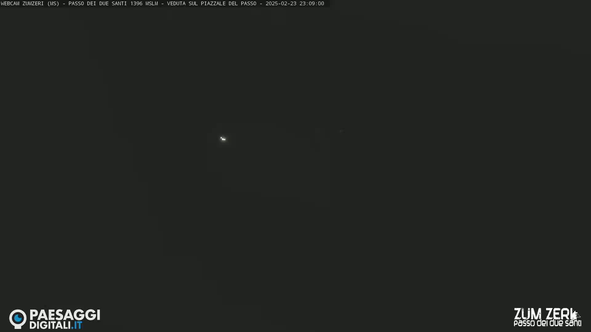 A dark, night-time scene shows a few faint lights in the distance under a clear, dark sky.