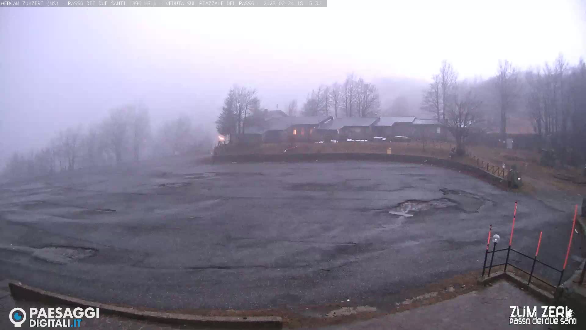 A foggy, overcast day reveals a large, damaged asphalt area with a building complex in the background.