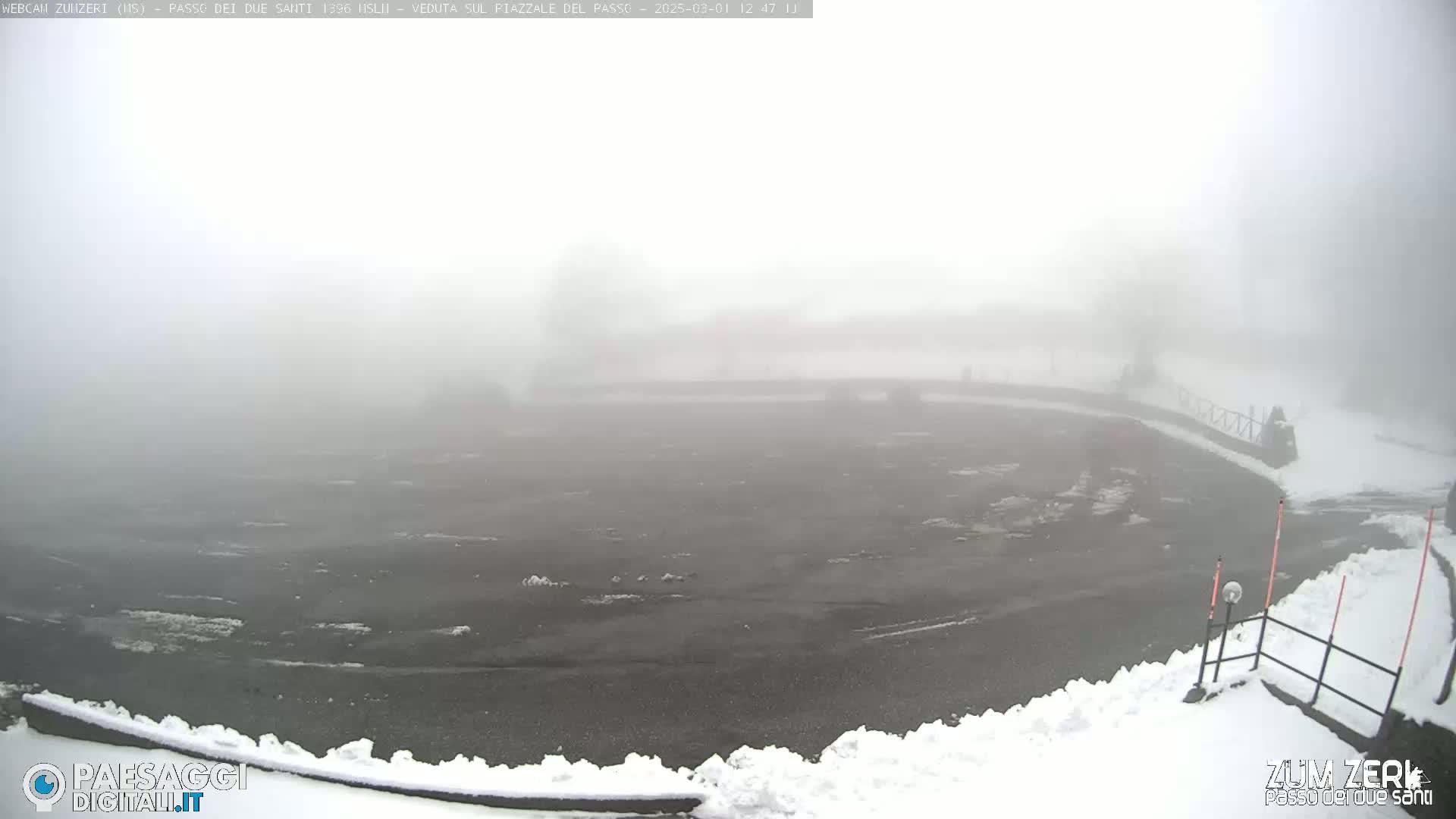 A foggy, snow-covered parking lot is visible, with a low-lying fence and some poles along the edges.