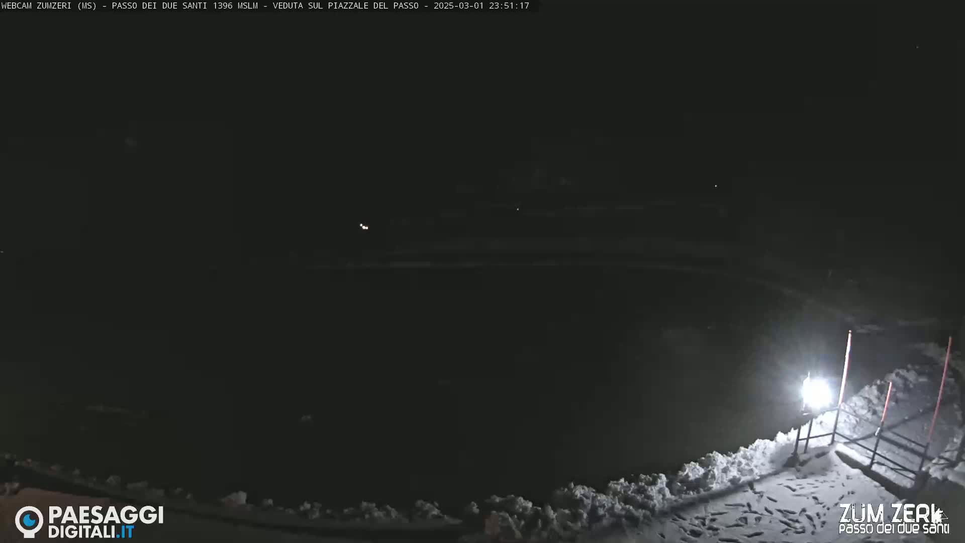 A dark, snow-covered area is illuminated by a single light at night.