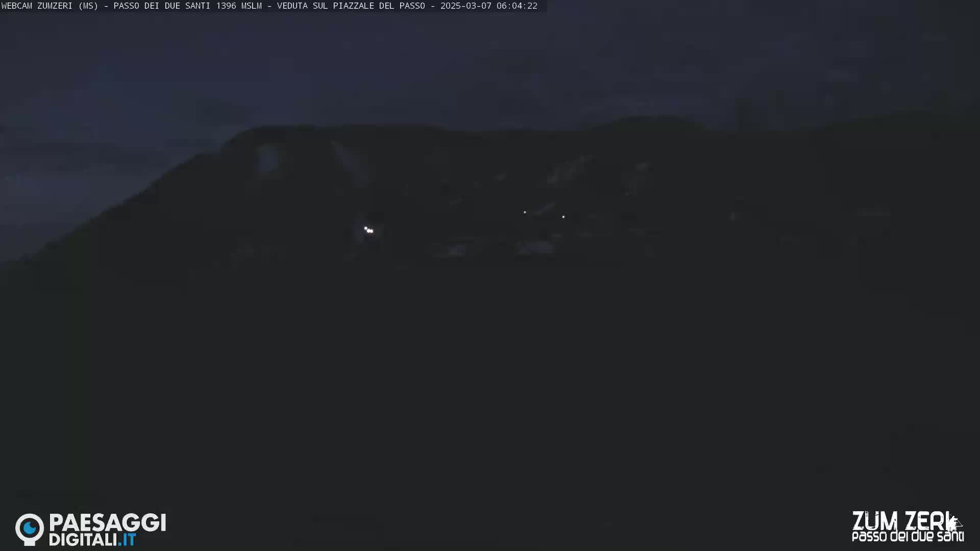 A dark, nighttime view of a mountainside with a few faint lights visible in the distance.