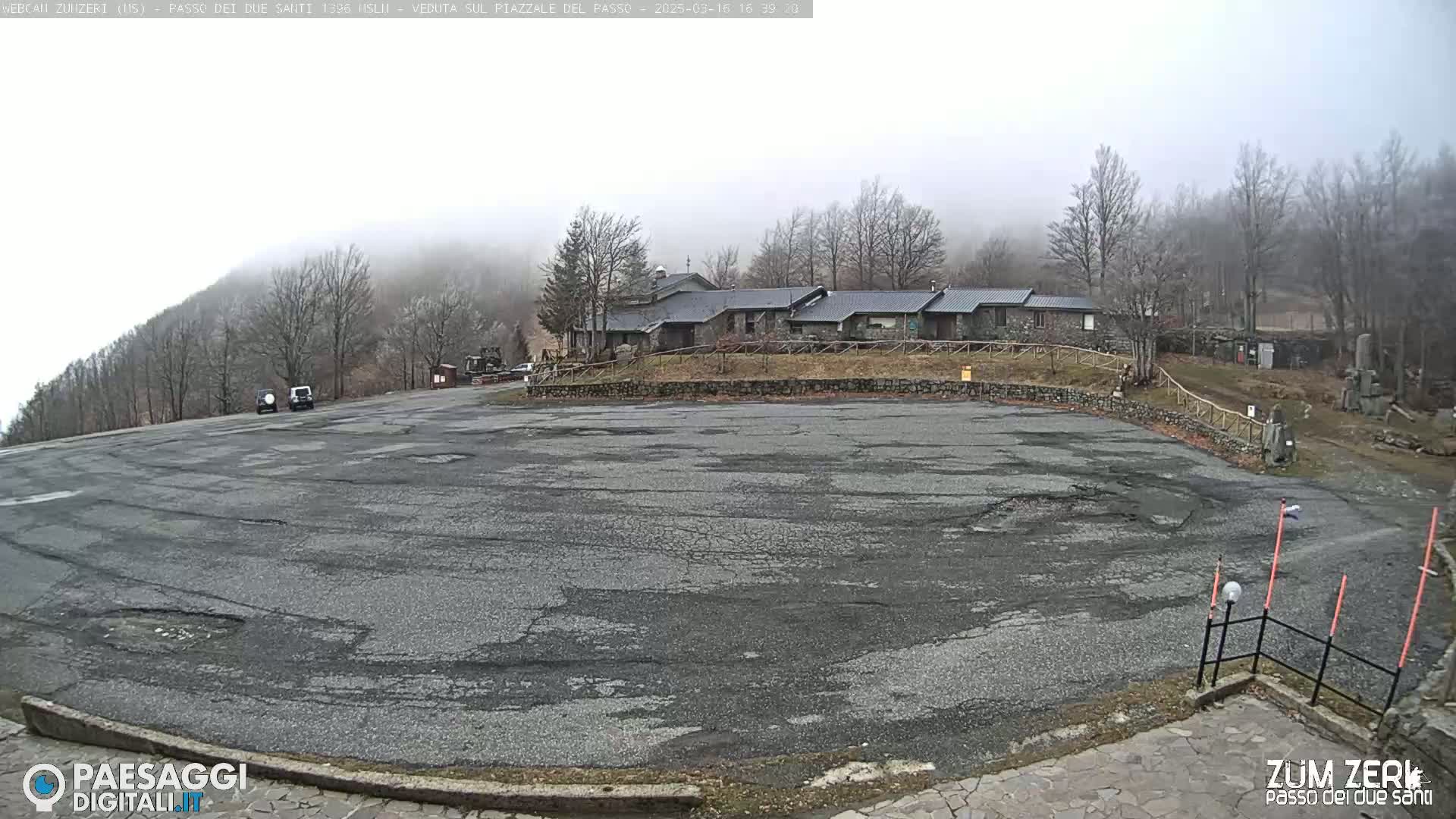 A large, cracked asphalt parking lot sits in front of a stone building complex under a foggy sky.