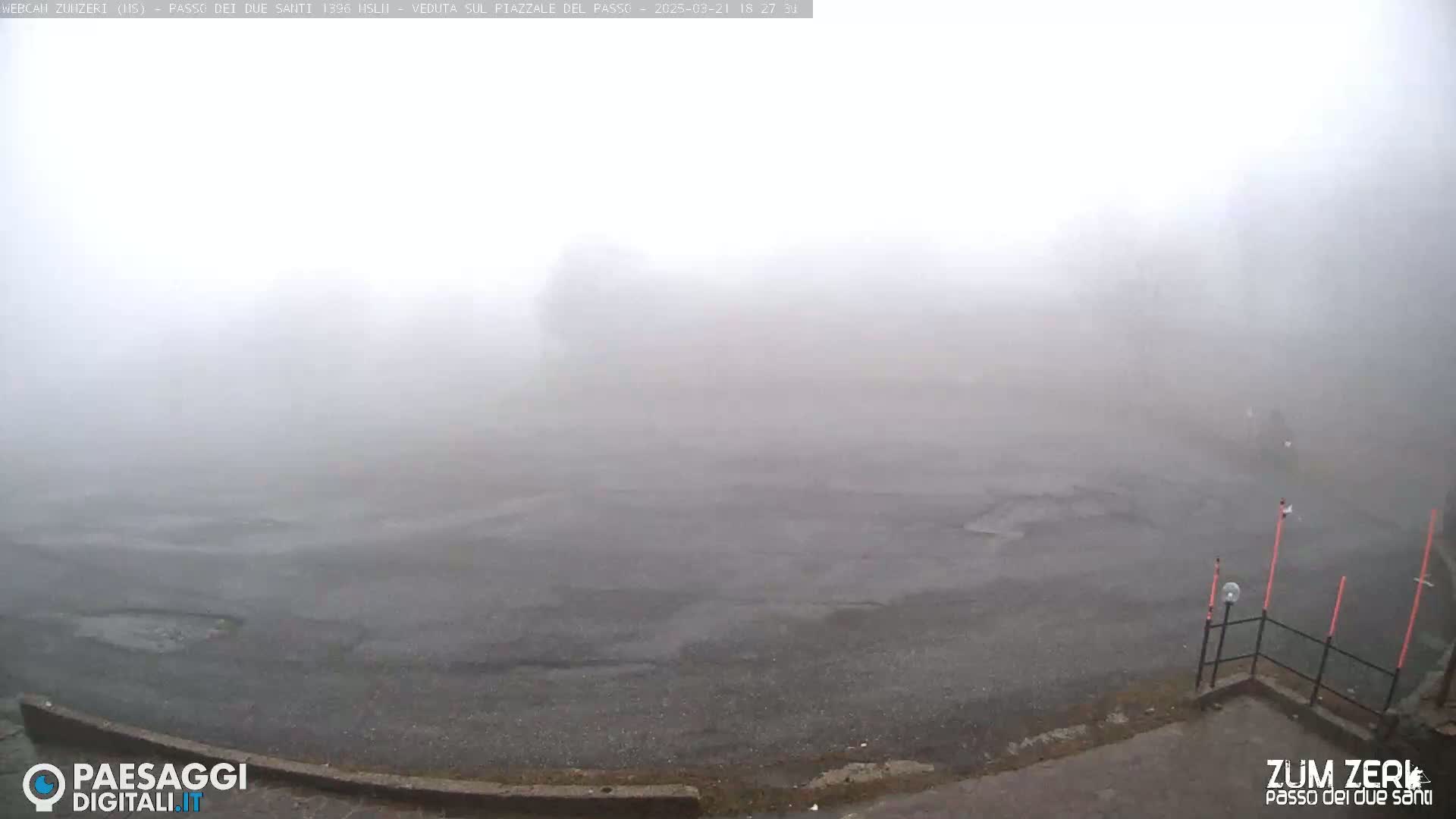 A foggy, paved area is visible, with a low fence and markers in the lower right corner.