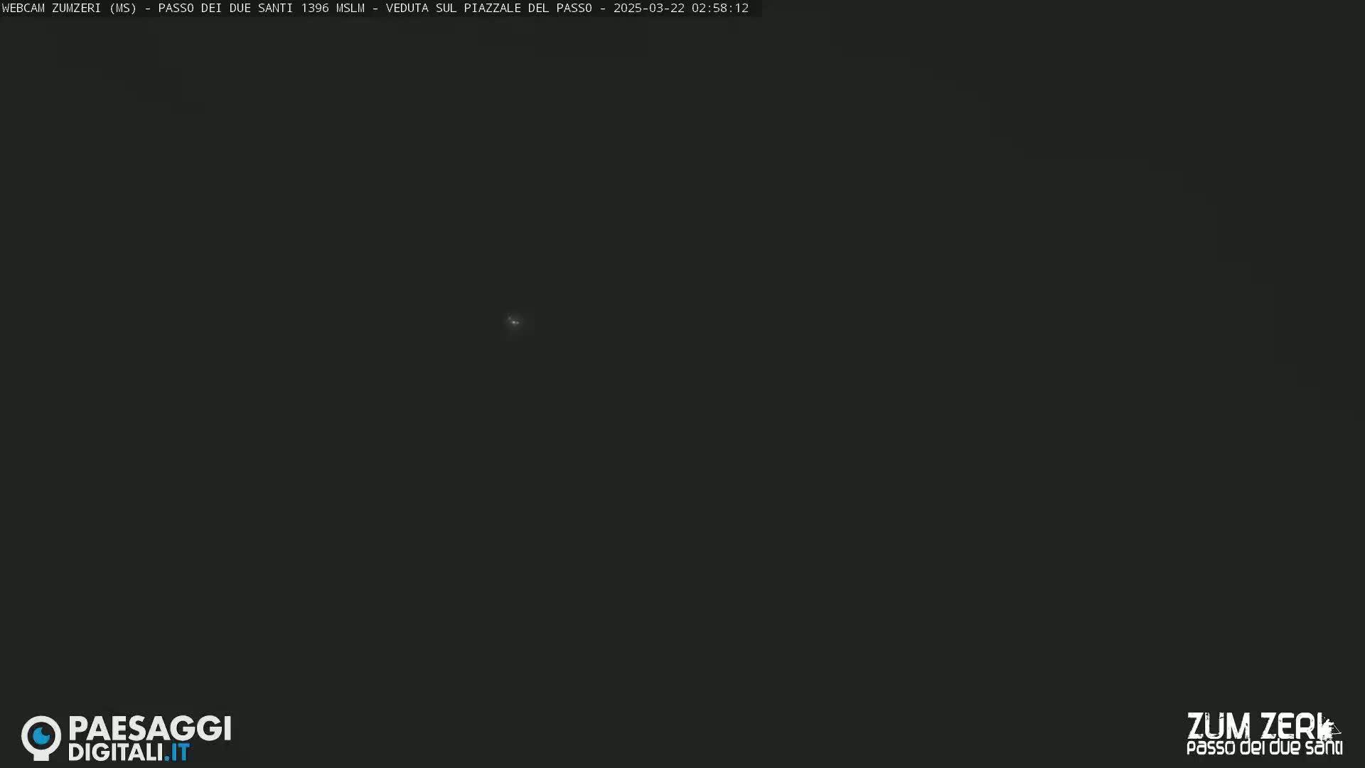 A dark, nighttime outdoor scene shows a very faint light source in the center.