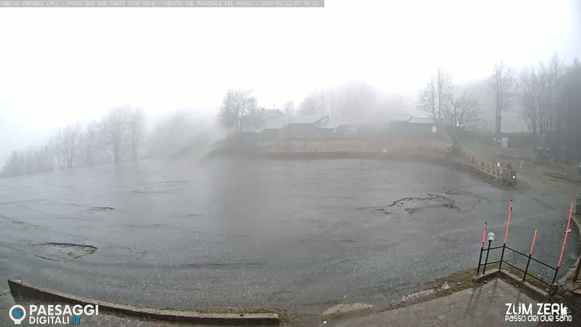 A foggy, wet parking lot is visible, with a few buildings and trees partially obscured by the mist in the background.