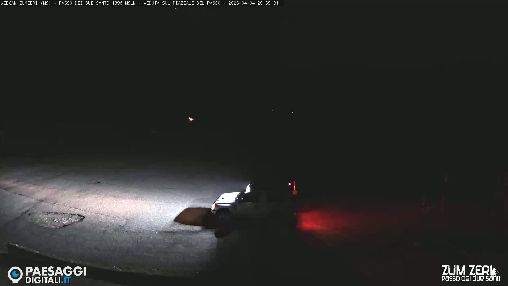 A light-colored vehicle is parked on a dark asphalt area at night.