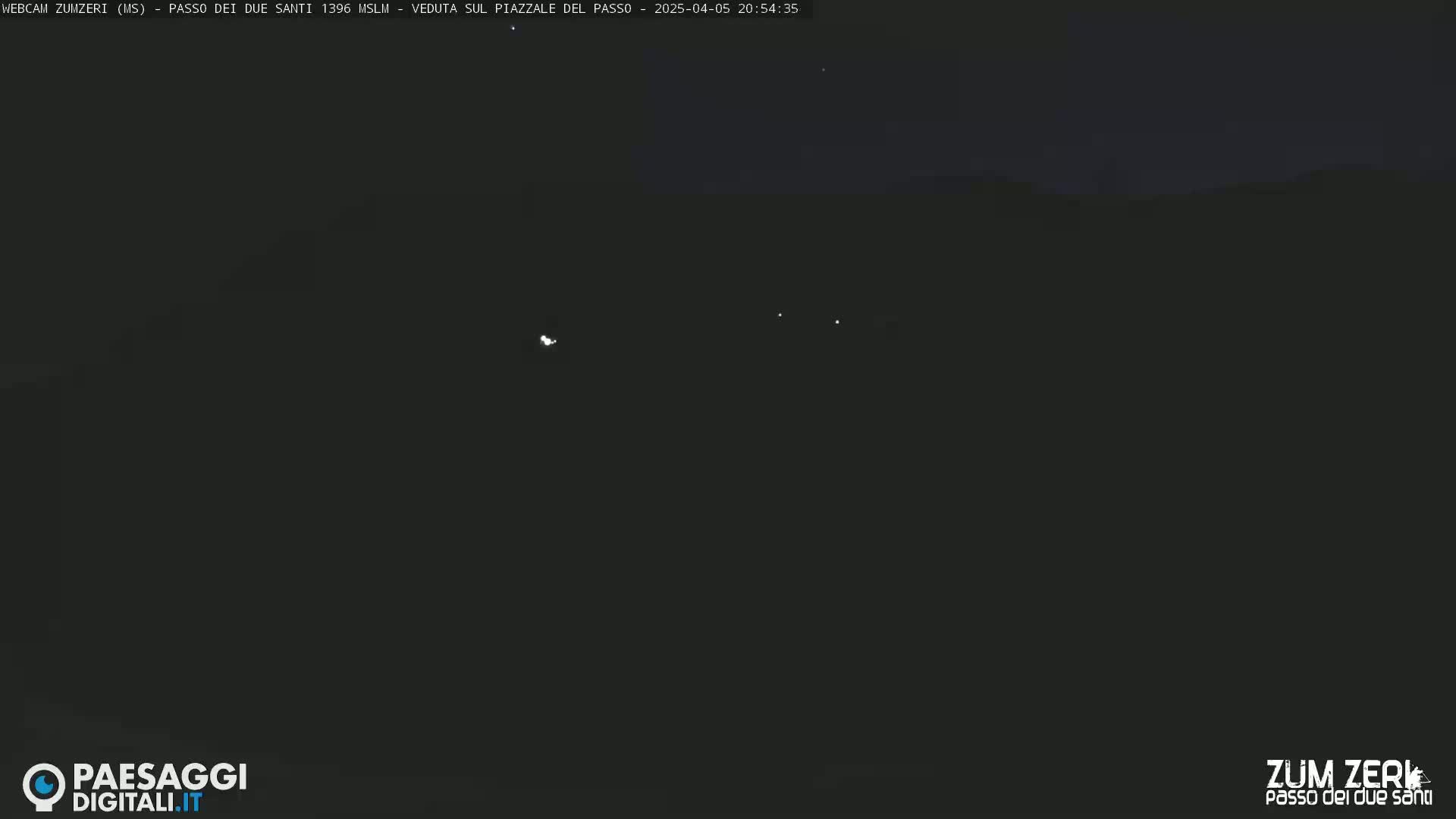 A dark, nighttime outdoor scene shows a few distant, faint lights against a mostly black sky.