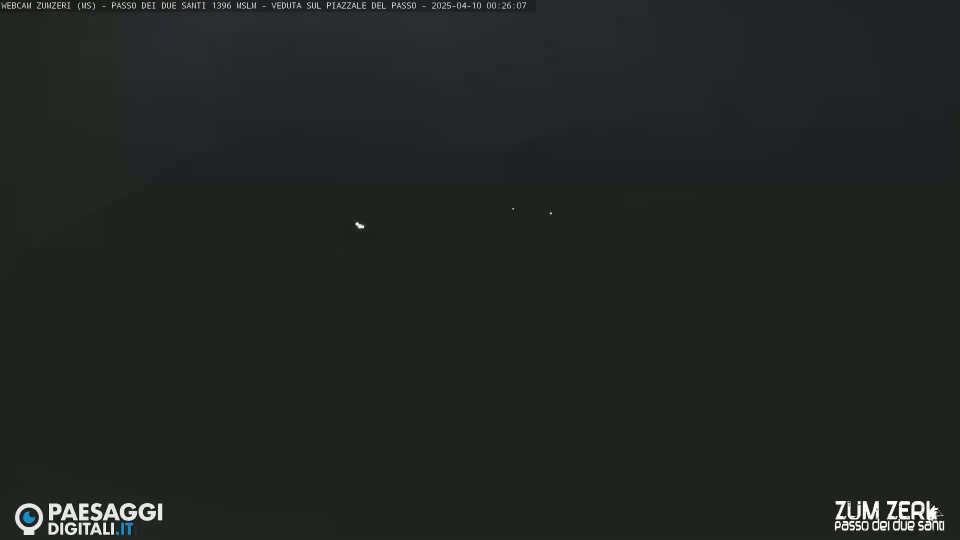 A dark nighttime scene shows a few faint lights in the distance under a clear sky.