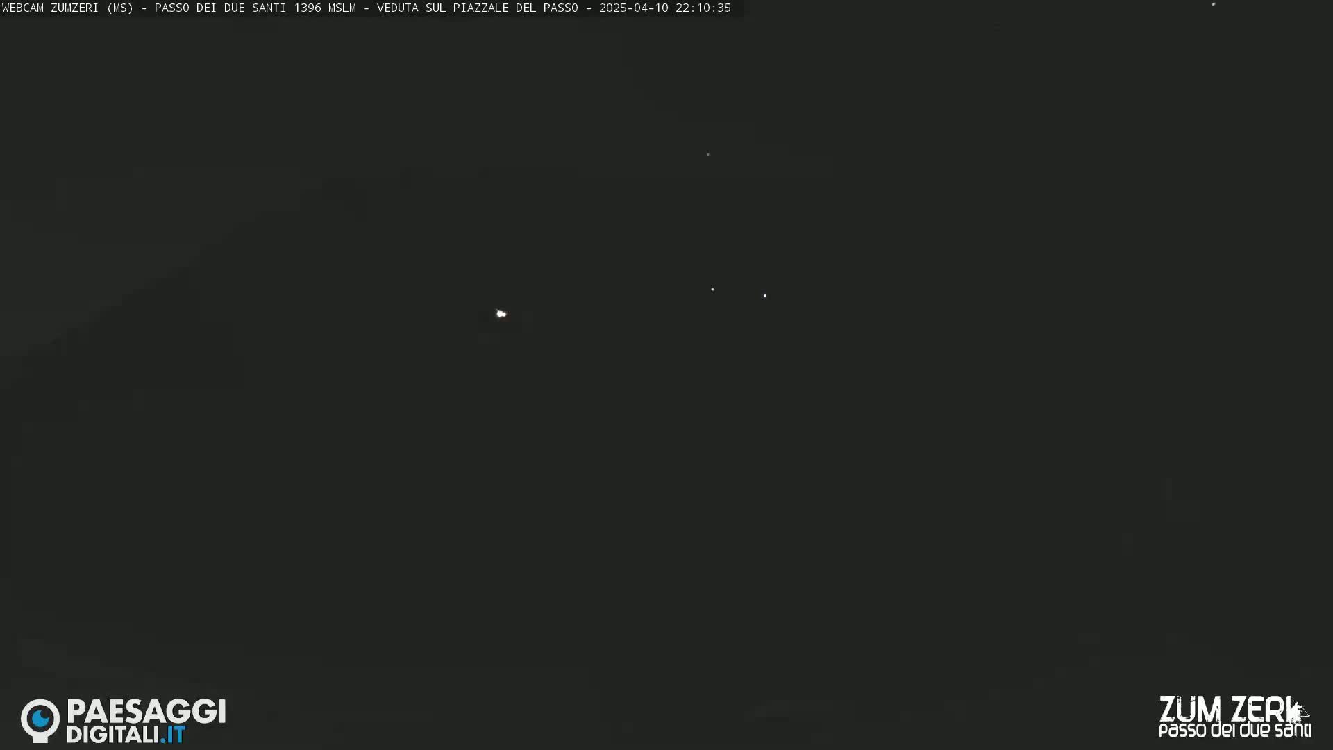 A dark, nighttime scene shows a few faint lights in the distance under a clear sky.