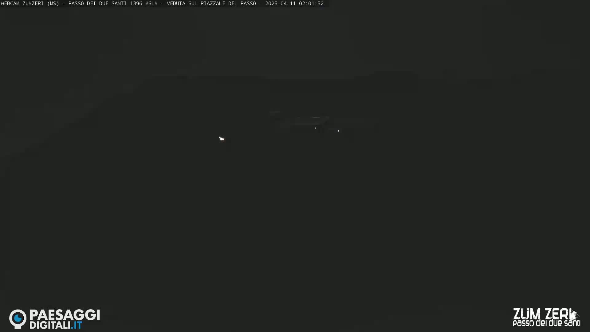A dark, nighttime scene shows a few faint lights in the distance.