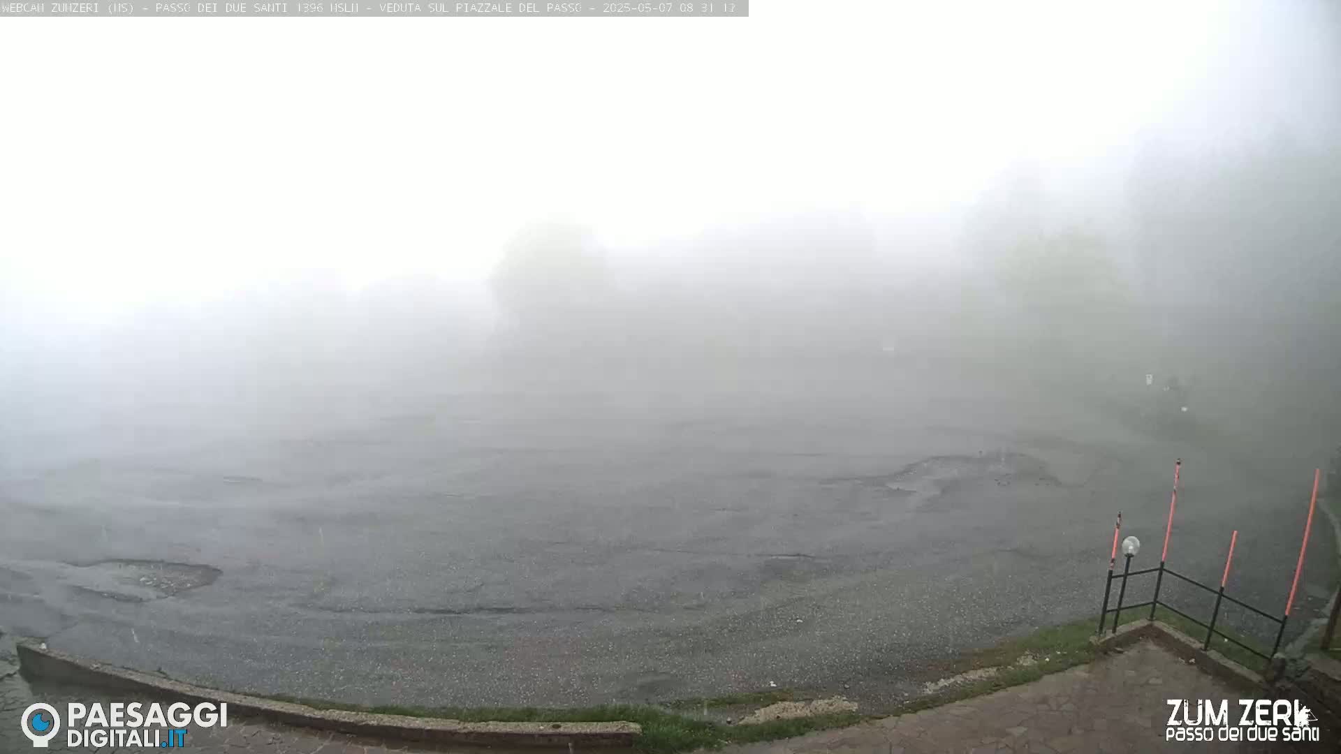 A mostly empty, wet asphalt area is shrouded in dense fog.