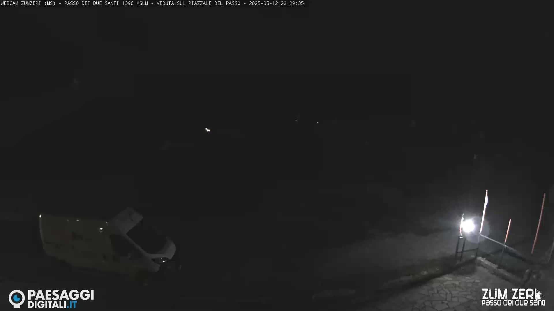 A white van is parked at night in a dark, empty square, illuminated by a single light source.
