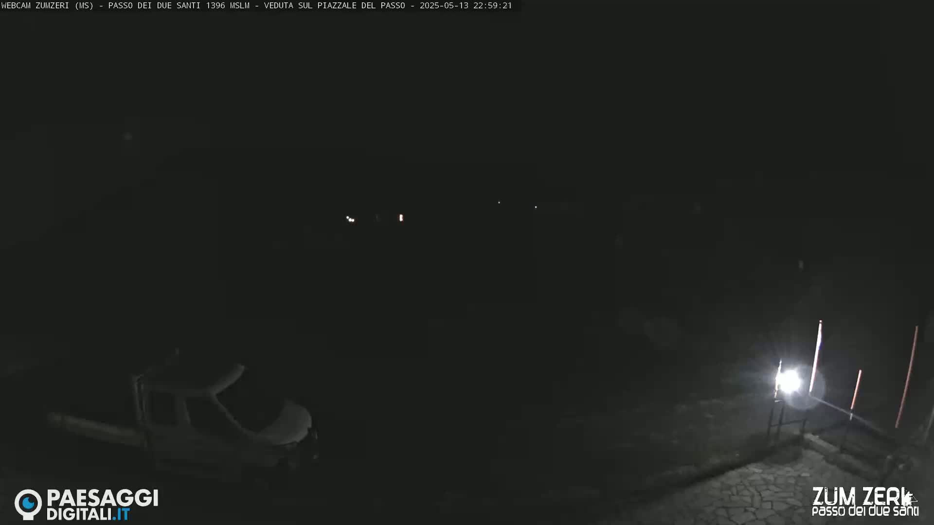 A dark nighttime scene shows a van parked in a mostly empty, paved area illuminated by a single bright light.