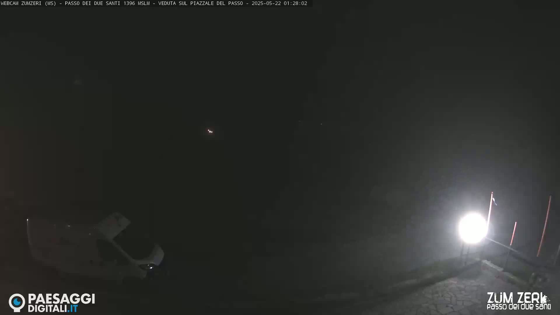 A nighttime, foggy scene shows a white van parked near a brightly lit area with some poles.