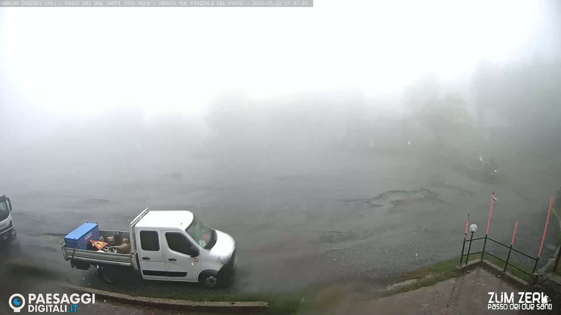 A white van is parked on a wet, foggy road near some trees.