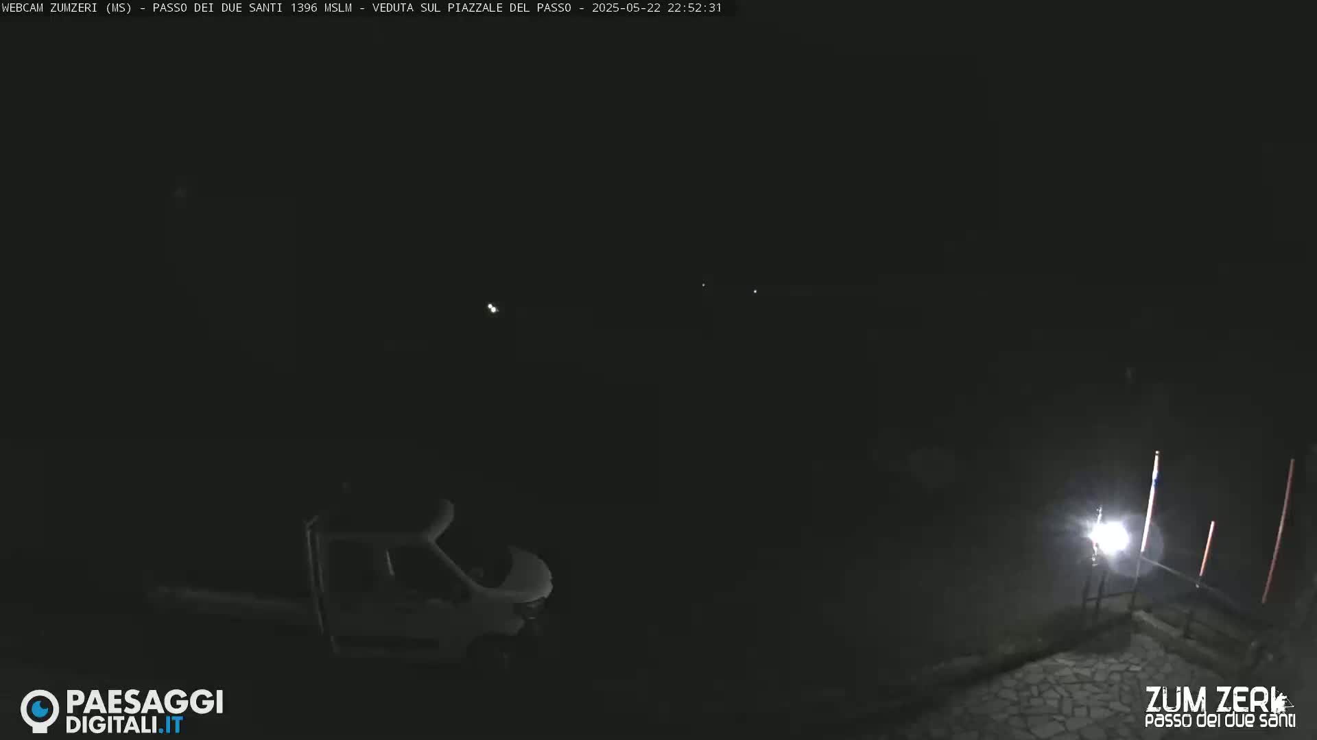 A white van is parked in a dark, nighttime outdoor scene illuminated by a single light source.