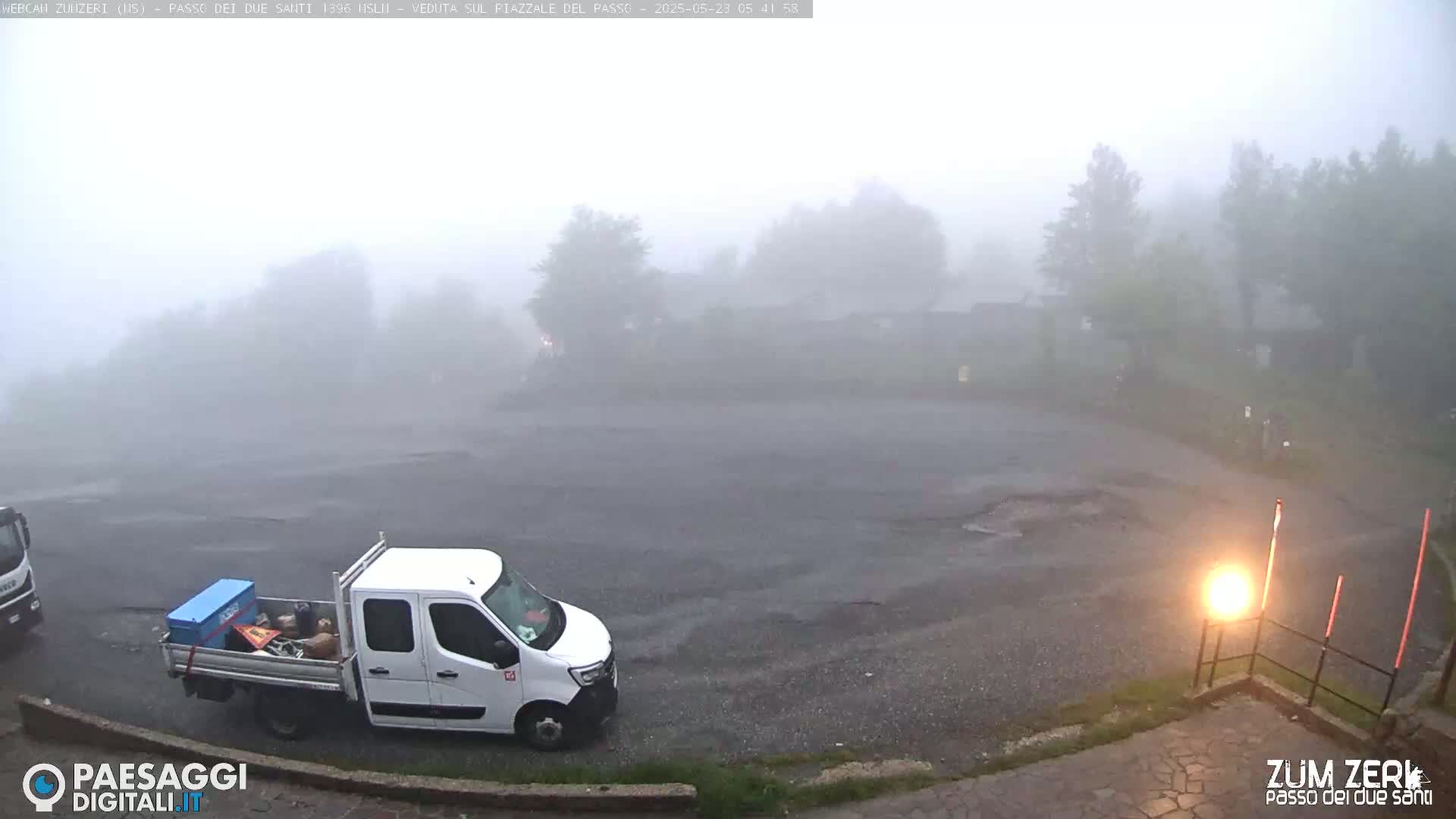 A foggy, rainy parking lot is shown with a white pickup truck and another vehicle partially visible in the distance.