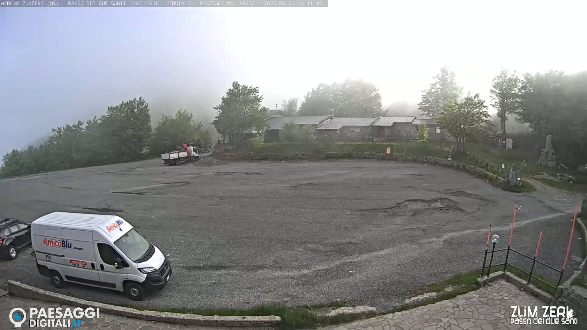 A foggy mountain parking lot with a few vehicles and buildings in the background.