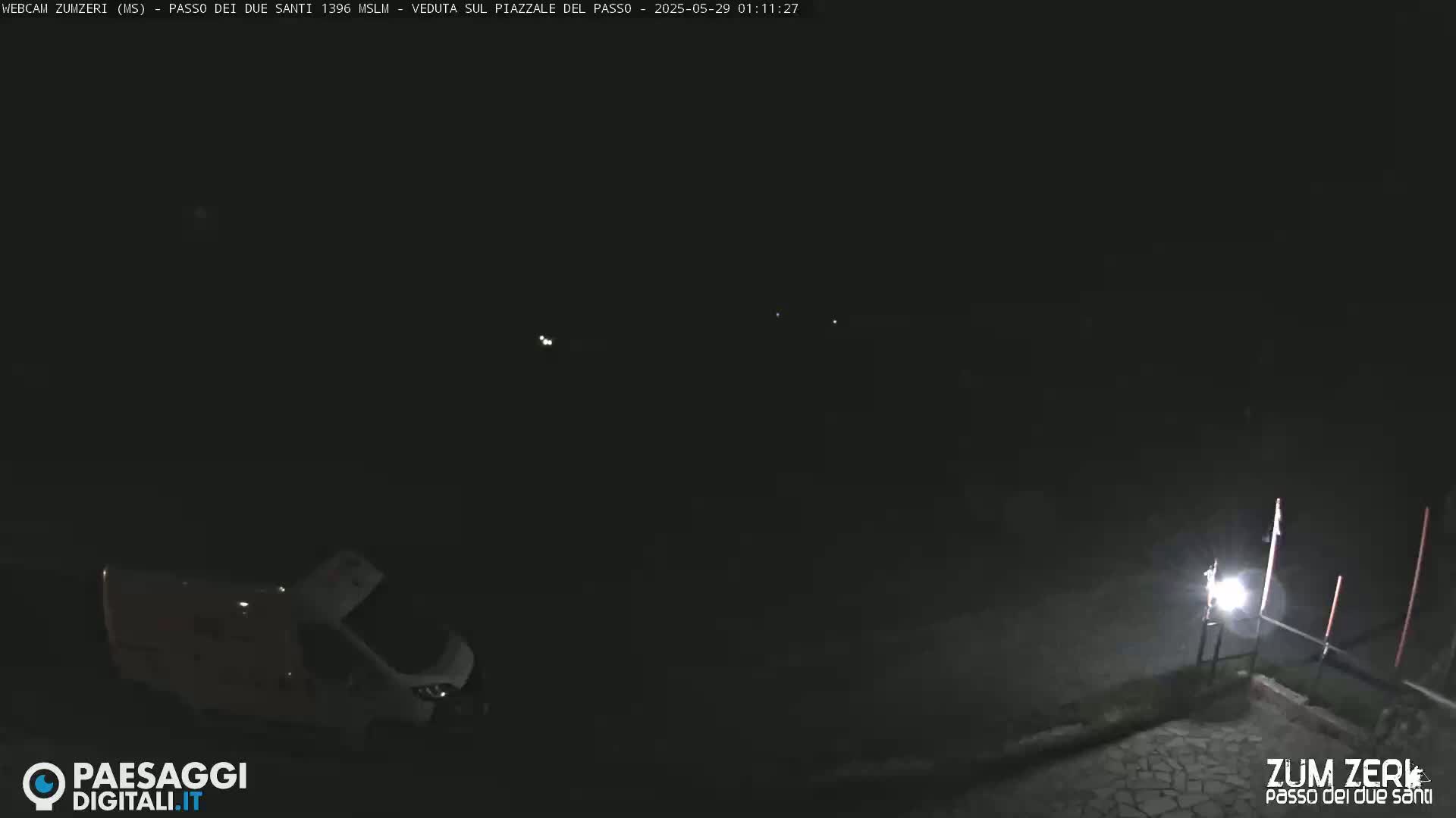 A van is parked in a dark, nighttime scene with a single light illuminating part of a paved area.