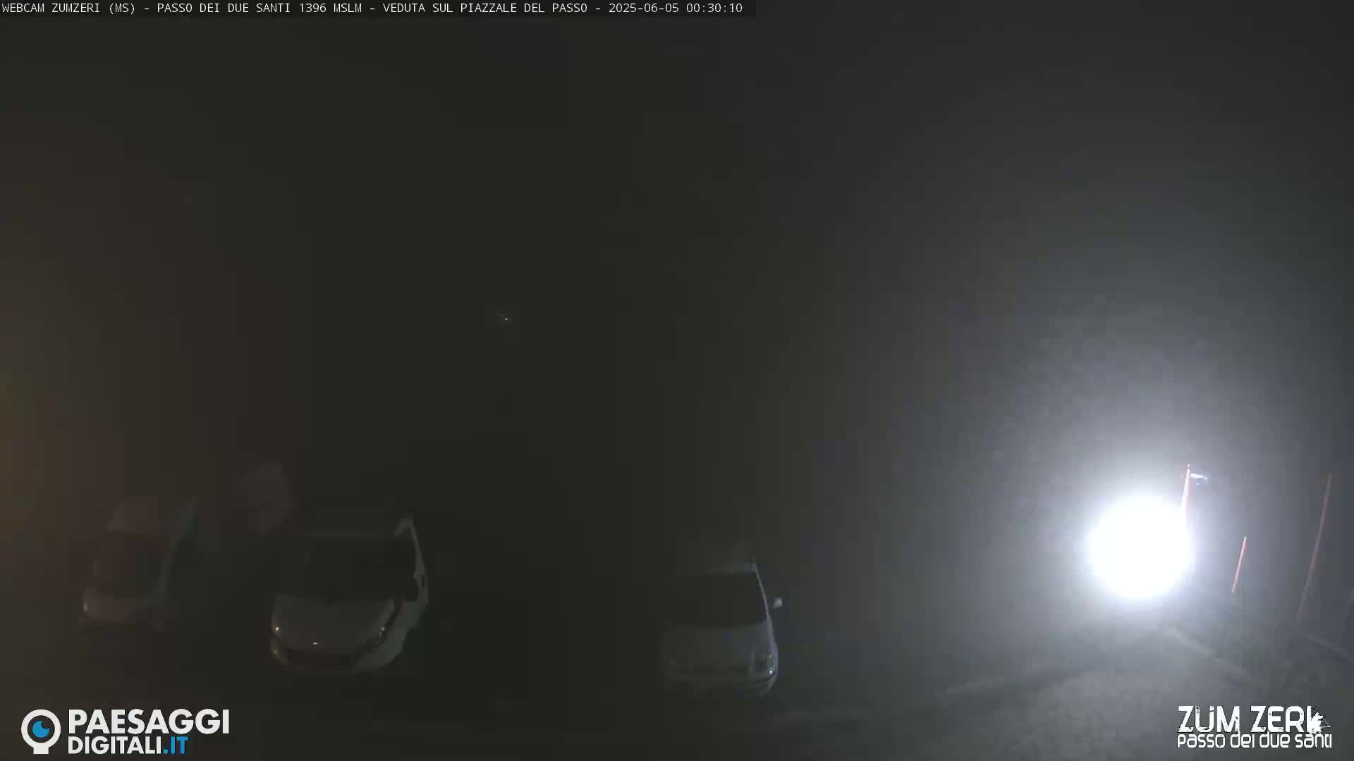 Three cars are parked in a foggy, dimly lit area at night.