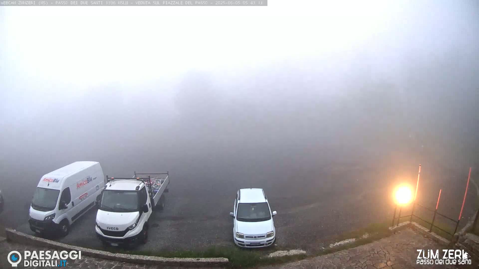 A foggy parking lot contains three white vehicles: a van, a flatbed truck, and a car.