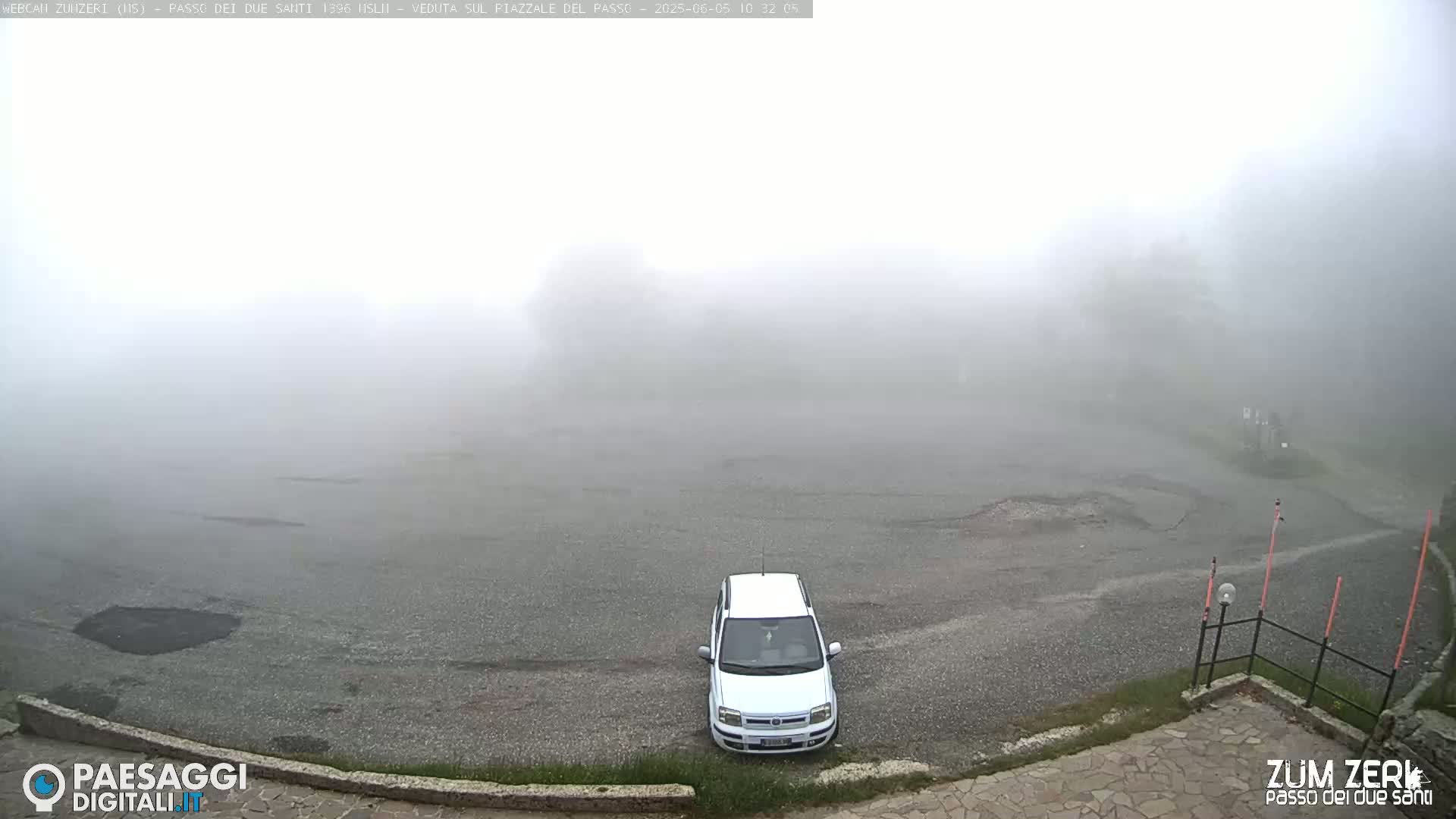 A white car sits in a foggy parking lot.