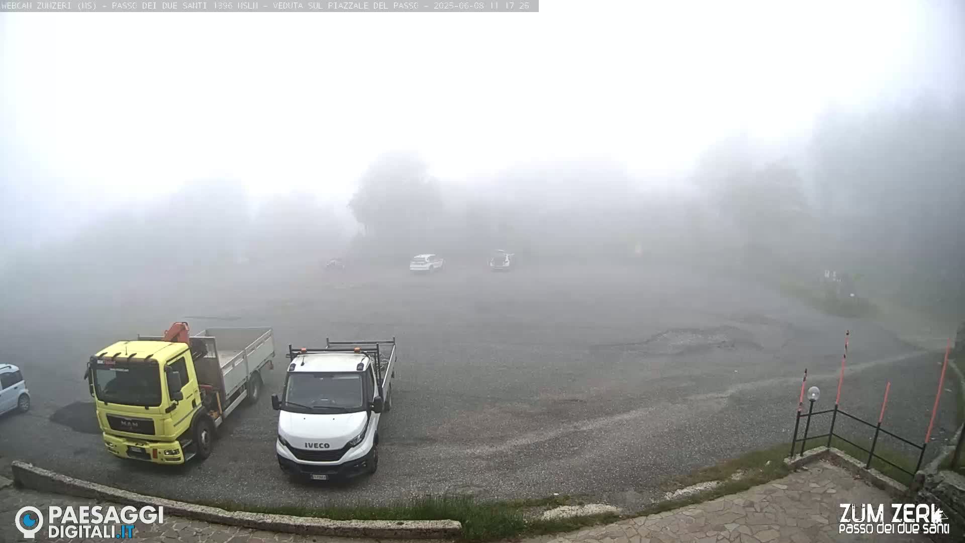 A foggy parking lot with several vehicles, including two trucks and a few cars, is shown.